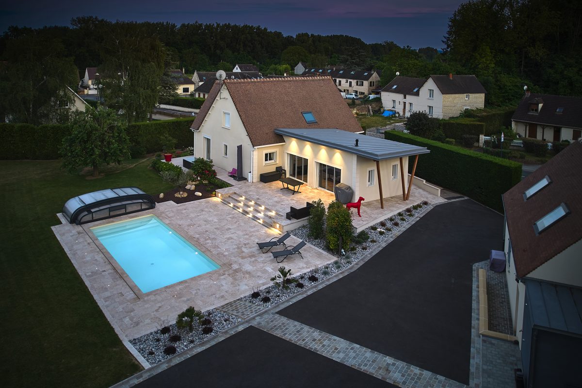 Piscine extérieure de nuit avec un lien uni sable et des margelles en travertin beige