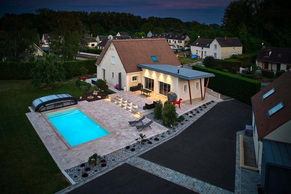Piscine extérieure de nuit avec un lien uni sable et des margelles en travertin beige