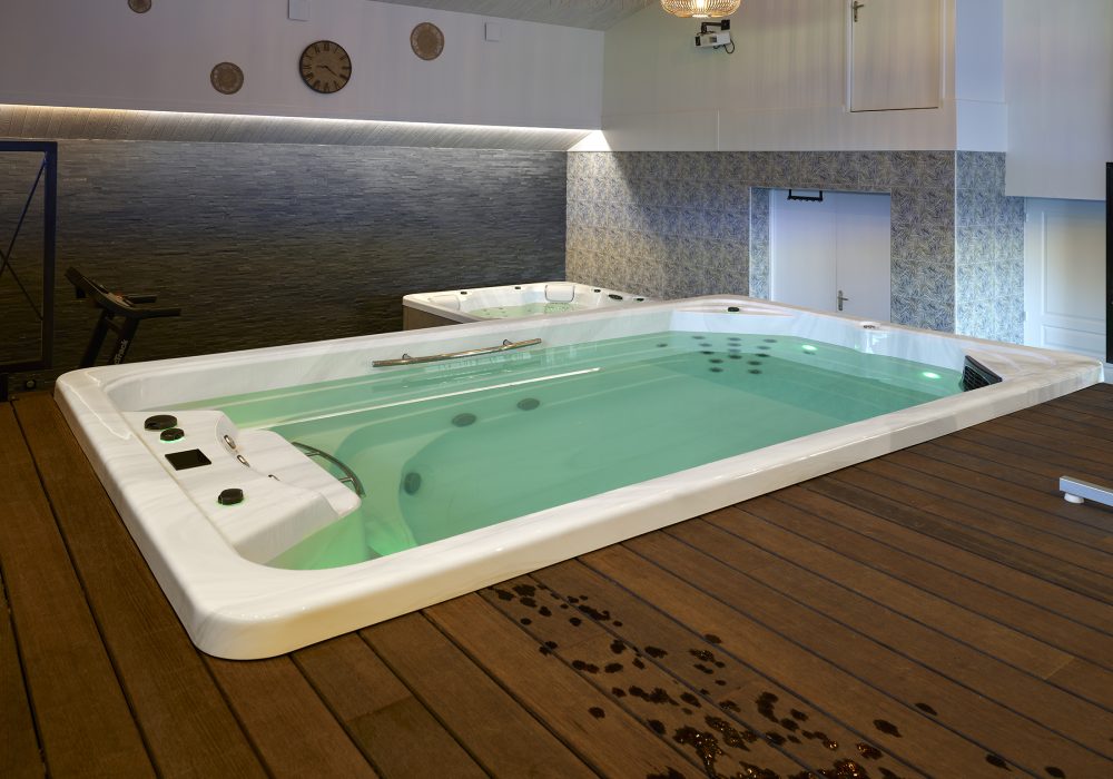 Espace intérieur combinant un jacuzzi et un spa de nage encastré pour la détente et l’exercice.
