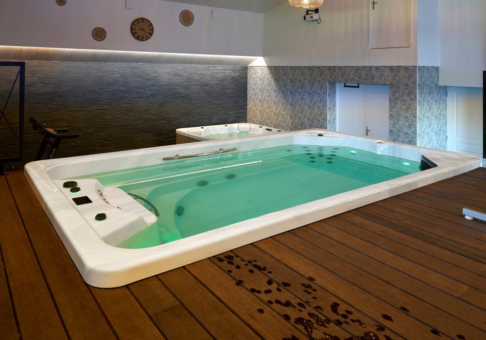 Espace intérieur combinant un spa à jets massants et un spa de nage encastré pour la détente et l’exercice.