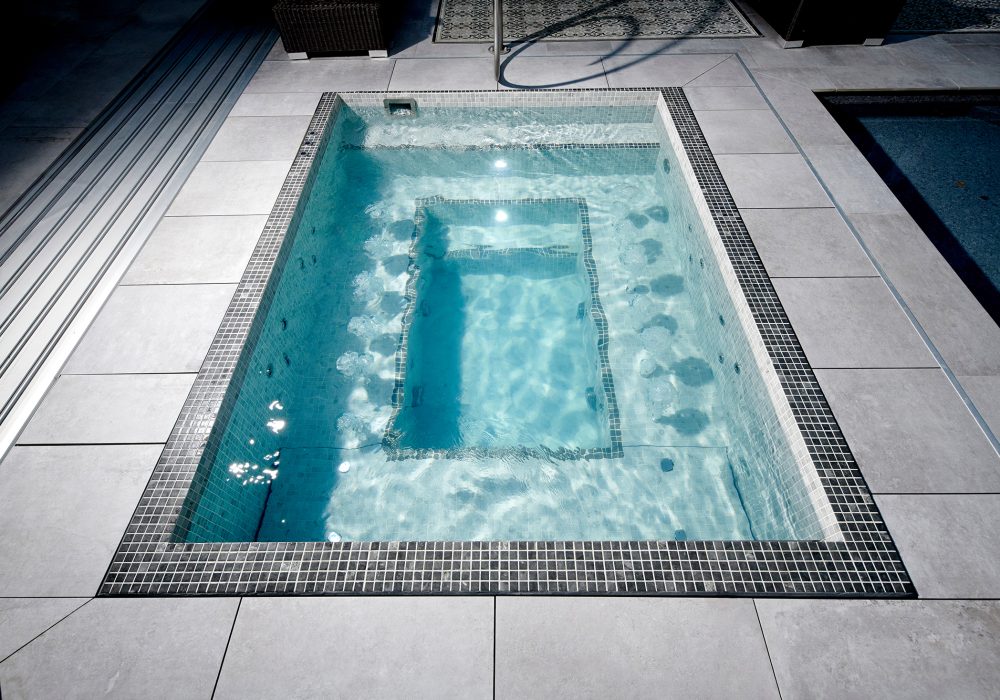 Spa sur mesure maçonné dans un espace piscine sous abri.